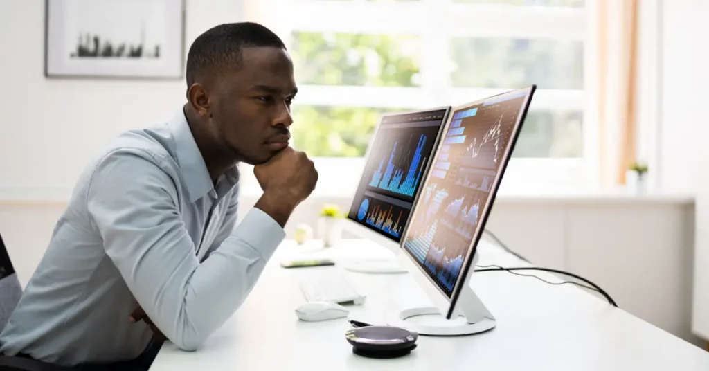 A man intently studying financial graphs on a computer monitor, suggesting focused analysis or decision-making. Budget Analyst Jobs