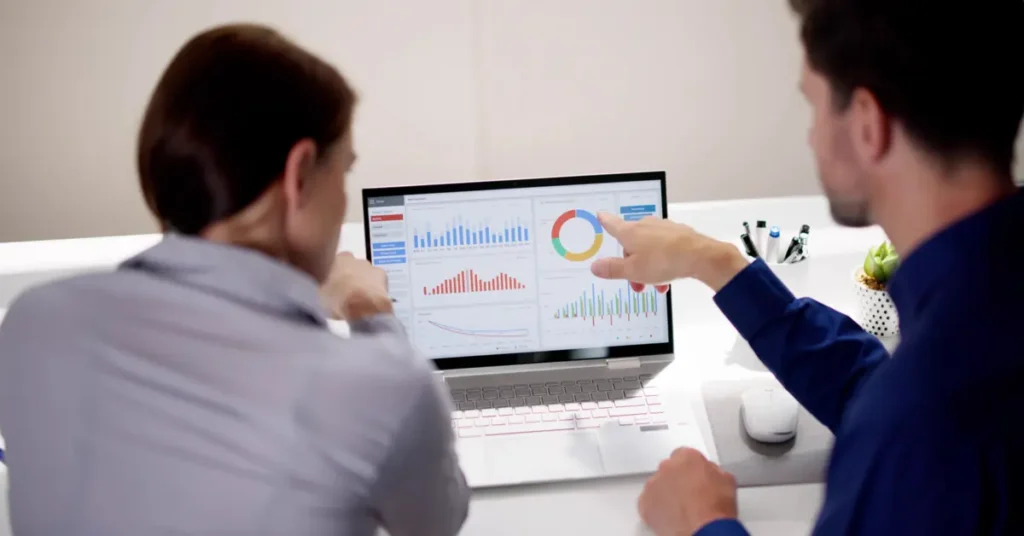 Two professionals discussing over a laptop with various charts on the screen, indicating collaboration and data analysis. Budget Analyst Jobs