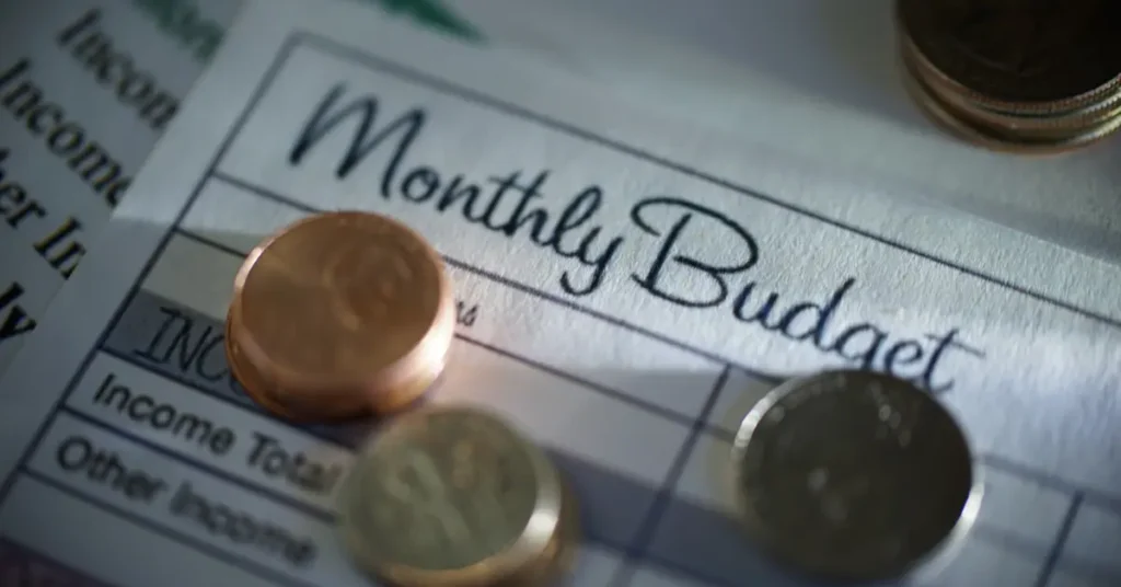 A close-up on a "Monthly Budget" sheet, highlighting attentive budgeting behavior with coins as financial symbols. Budgeting Behavior