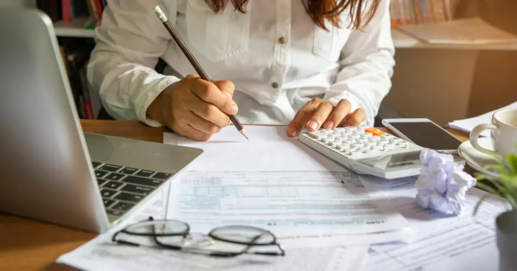 A woman working on financial documents with a calculator and laptop, exemplifying personal budget management. Budgeting for Dummies