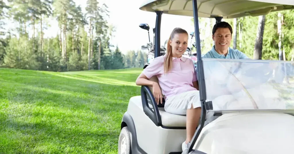 A smiling man and woman seated in a golf cart on a lush golf course.