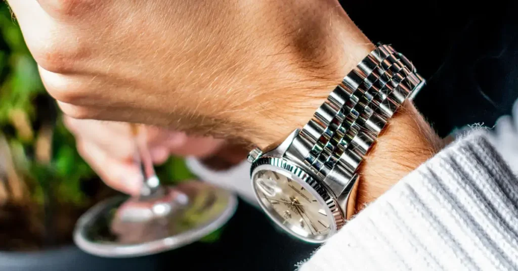 A person wearing a steel watch with a light face, checking the time while pouring a drink. Rolex financing is a way to buy such a watch